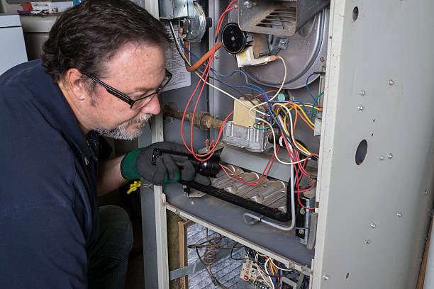 technician looking over a gas furnace with a flashlight before cleaning it.
